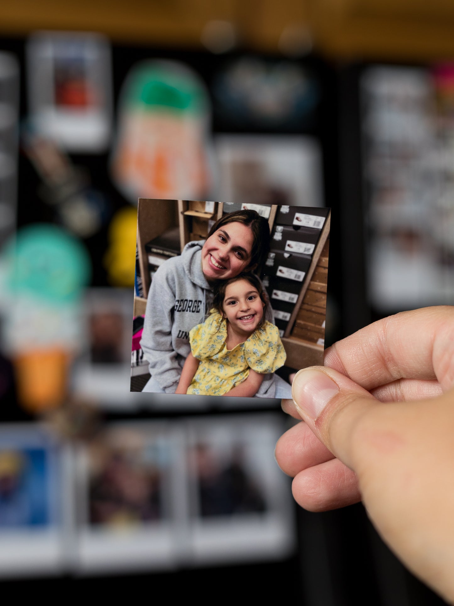 Hand holding a 2x2 custom magnet photo of a woman and a child in front of a blurred fridge.